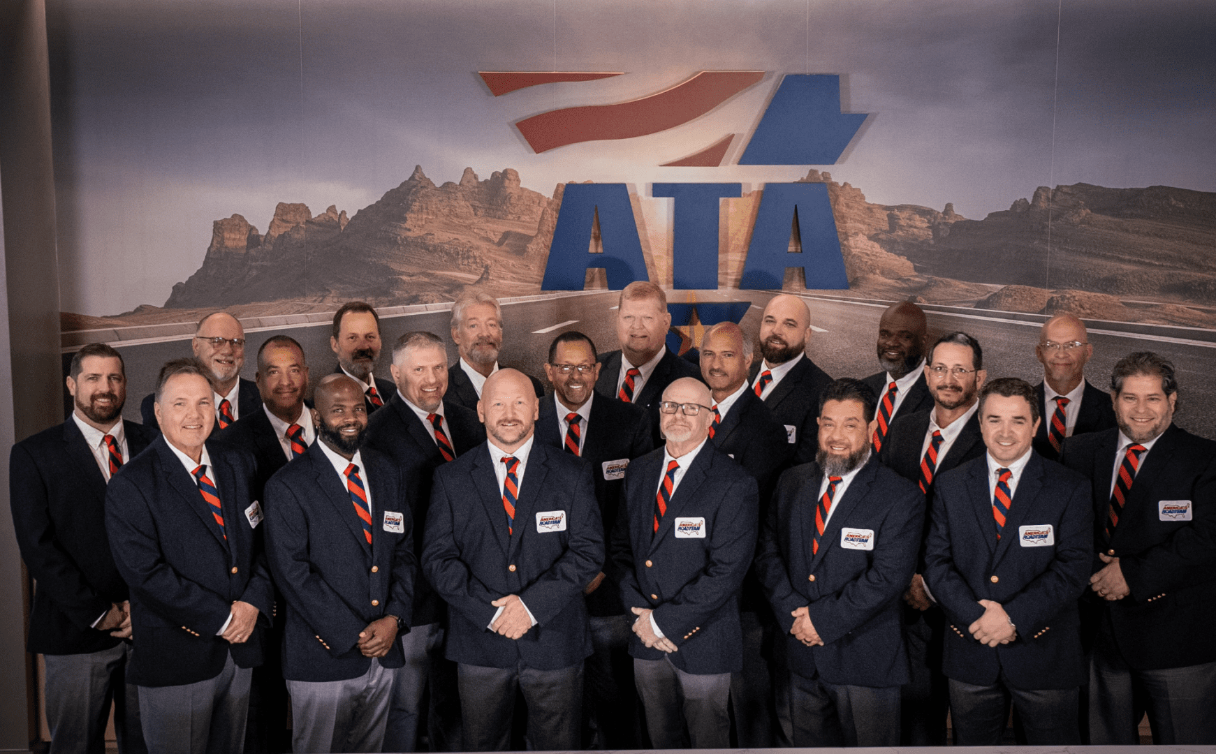 Group of ATA members posing in suits with a backdrop showing the ATA logo and mountains.